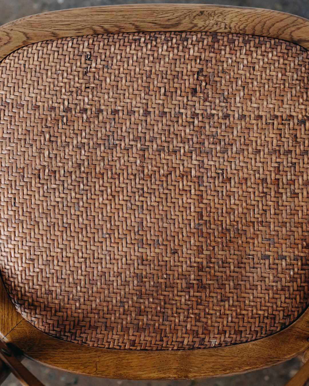 Close-up of a woven rattan or wicker chair back with a curved medium-brown wooden frame. Hamptons Natural Oak Dining Chair | Rustic Charm Interiors 