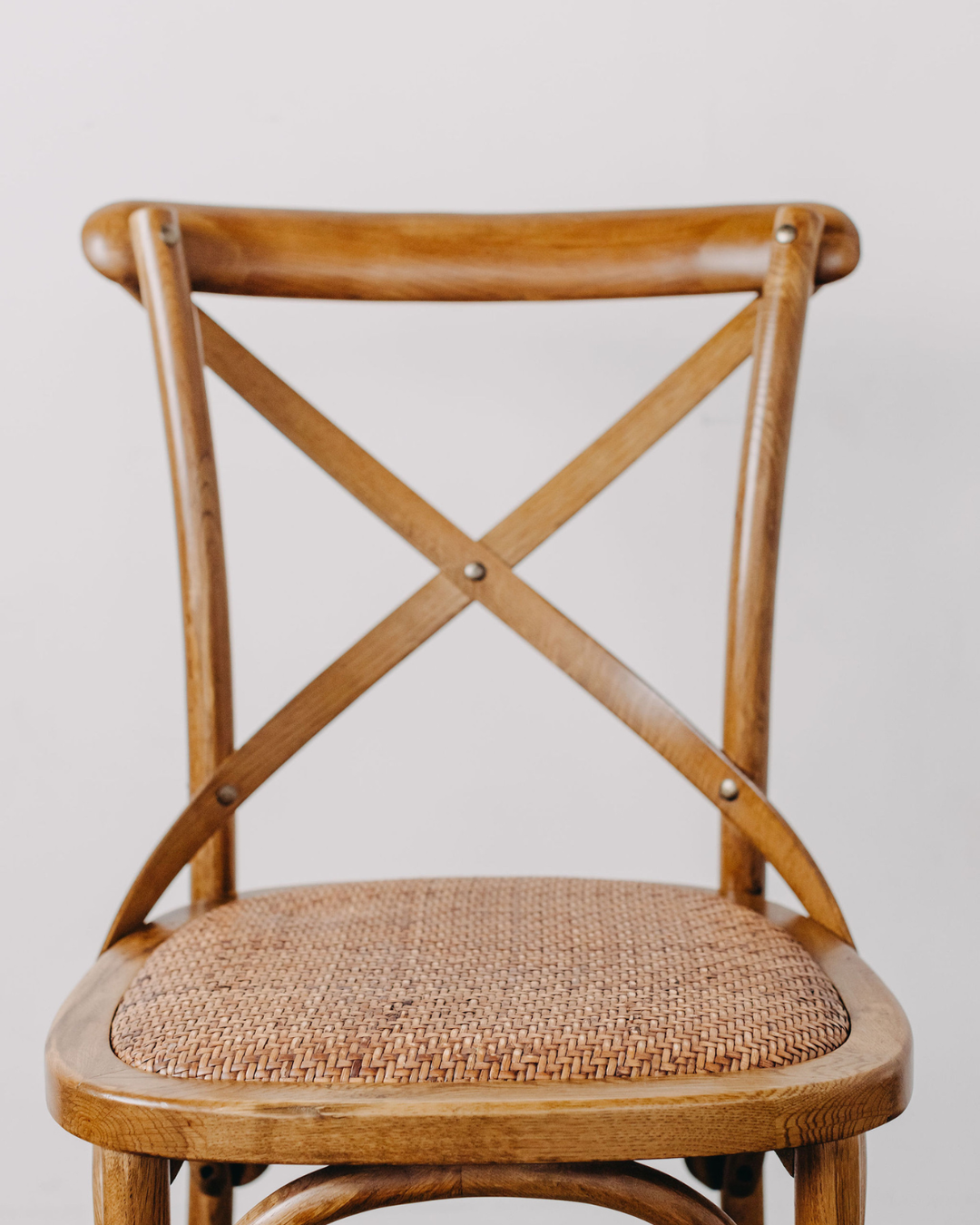 A close-up of a wooden dining chair with a natural cane seat and a curved wooden backrest featuring an X-back design.