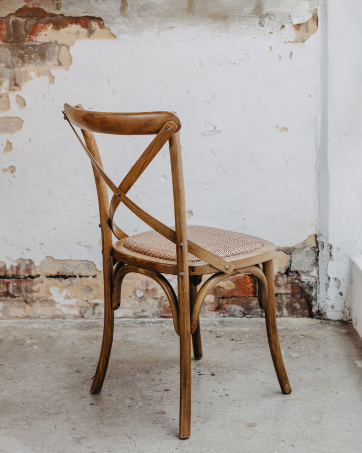 A classic wooden dining chair with a woven cane seat, positioned against a rustic white plaster wall with exposed brick detailing.
